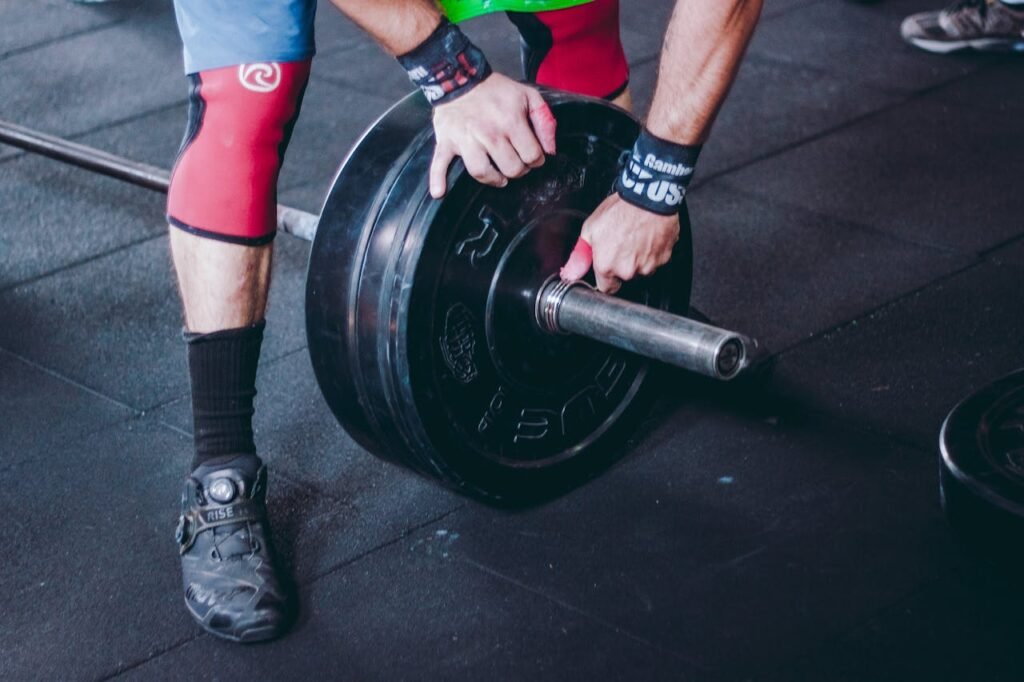 Person putting weighs on a barbell, on a gym floor.