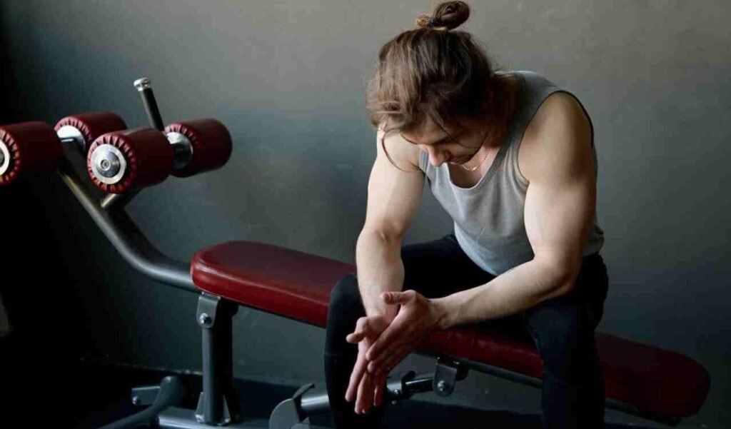 A person sitting down and looking defeated in a gym due to burnout.