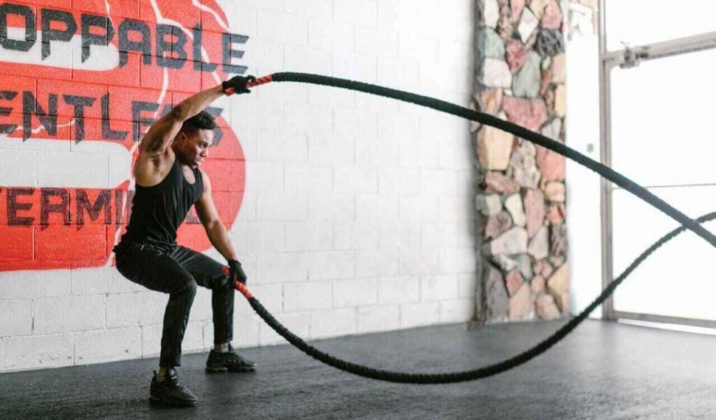 A guy in a gym, doing a work out with battle ropes.