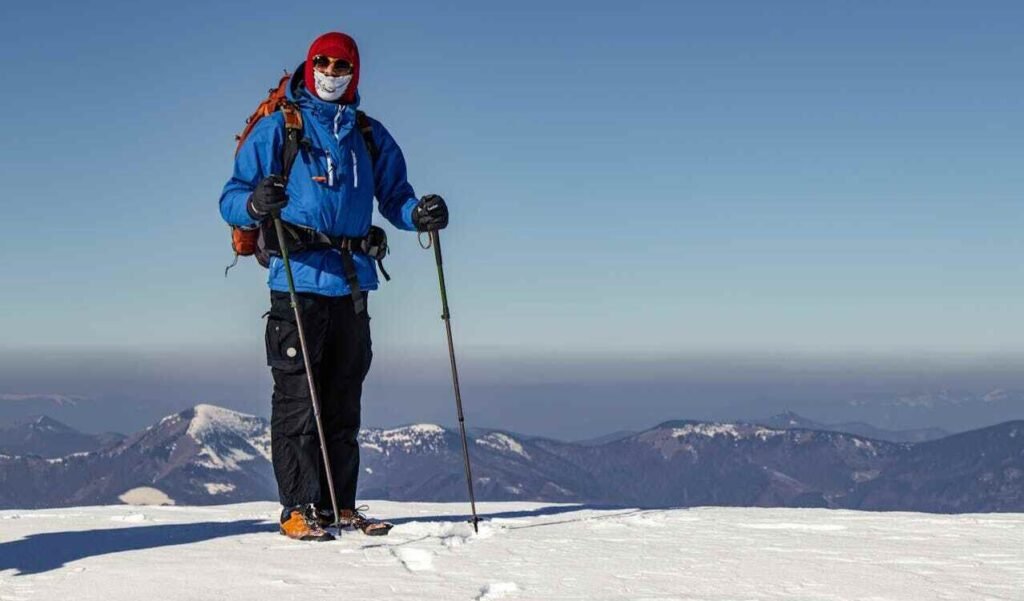 A person hiking up a mountain, which is covered in white snow and there are more big mountains in the distance and blue sky.