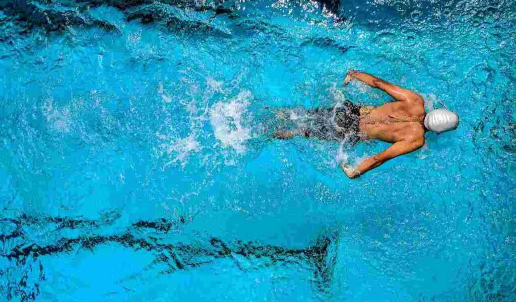 Person swimming, in a blue swimming pool as cardio exercise.