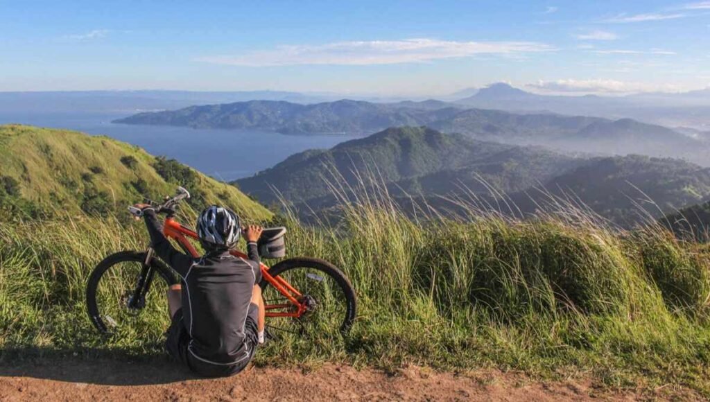 Mountain bike rider sitting down beside their bike, looking over at the mountains.