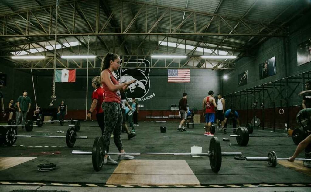 a woman in the foreground of a busy cross fit gym, with weights from the workout on the floor.