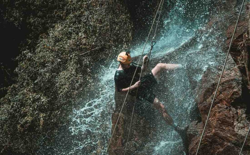 A person abseiling down a waterfall, showing raw fitness needed for canyoning.