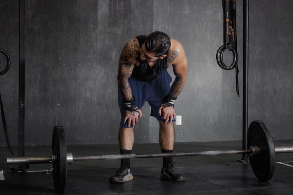 Guy at the gym bent over resting with weights on the ground.
