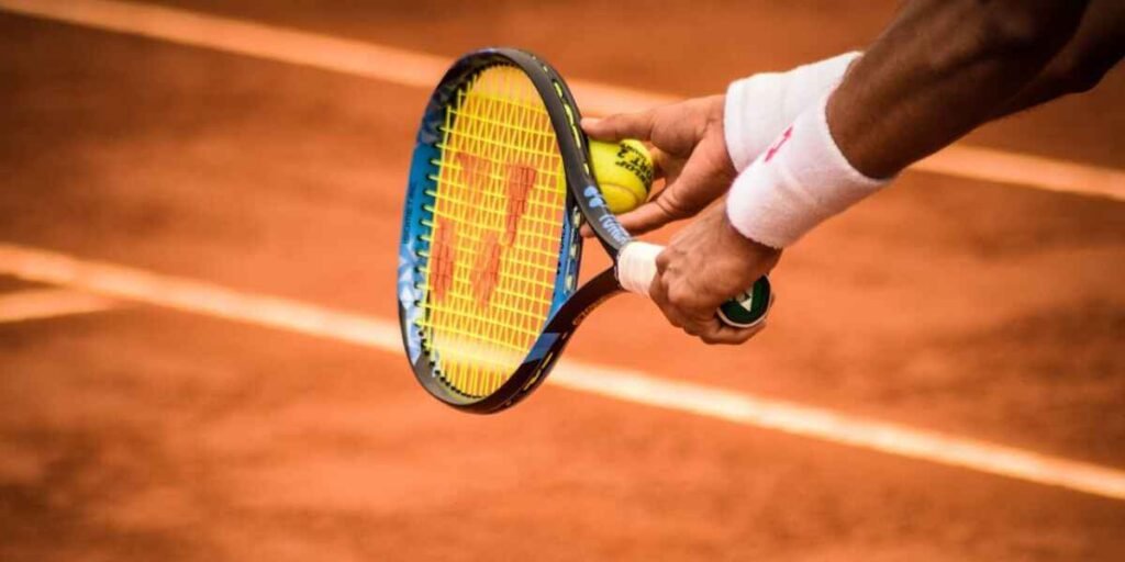 A person's hands holding a tennis racket and a tennis ball on a tennis court, as a form of cardio.