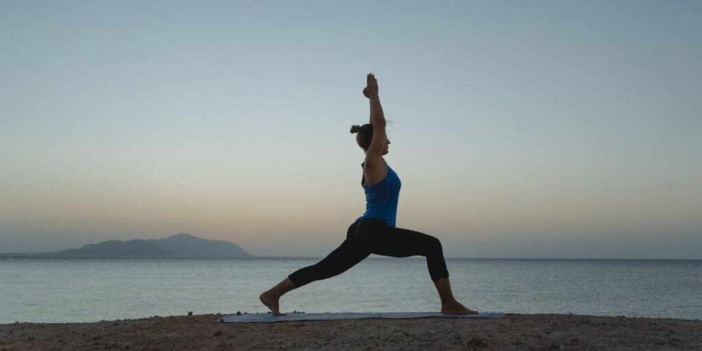 A woman doing yoga next to water with mountains in the distance, demonstrating flexibility and mobility.
