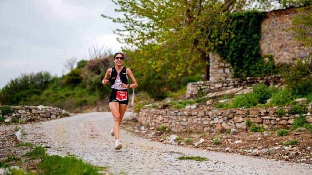 A woman running on a stone path, smiling and enjoying cardiovascular endurance.