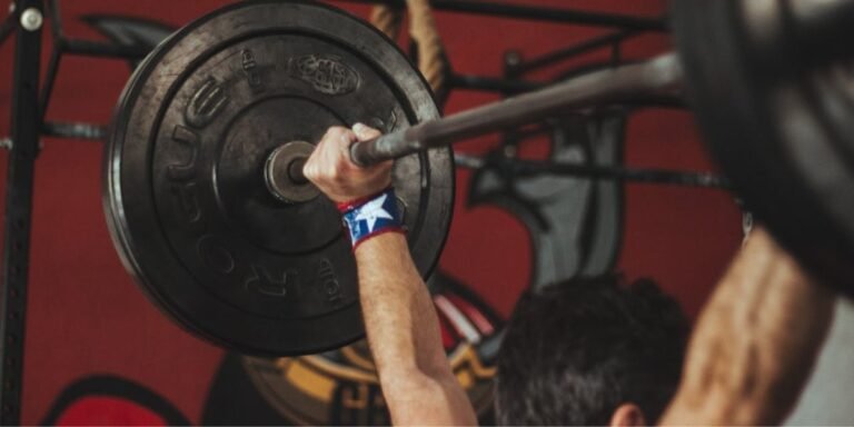 Guy in a gym lifting a barbell overhead, showing how to maintain fitness with strength training.