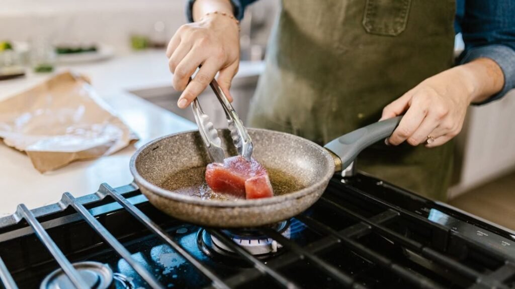 Female hands placing a chunk of fish into a hot frying pan, demonstrating cooking a protein-rich meal.