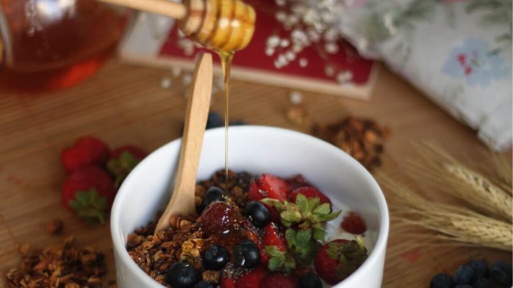 Protein snack with Greek yoghurt, granola, and berries, honey being drizzled on top reducing the protein-per-calorie ratio