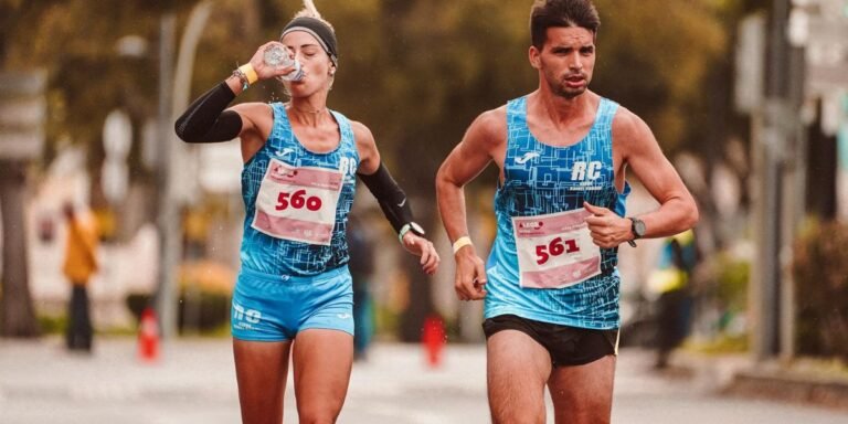 Two runners competing in a marathon, one drinking water while running to illustrate hydration during endurance exercise.