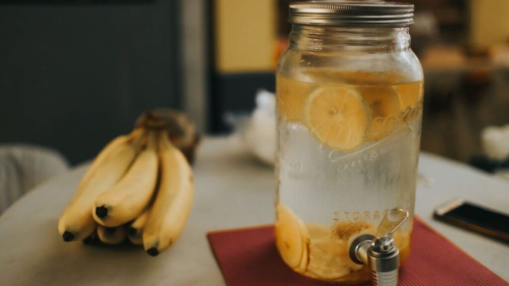 A container of lemon water in the foreground with bananas in the background, representing hydration and potassium-containing foods.