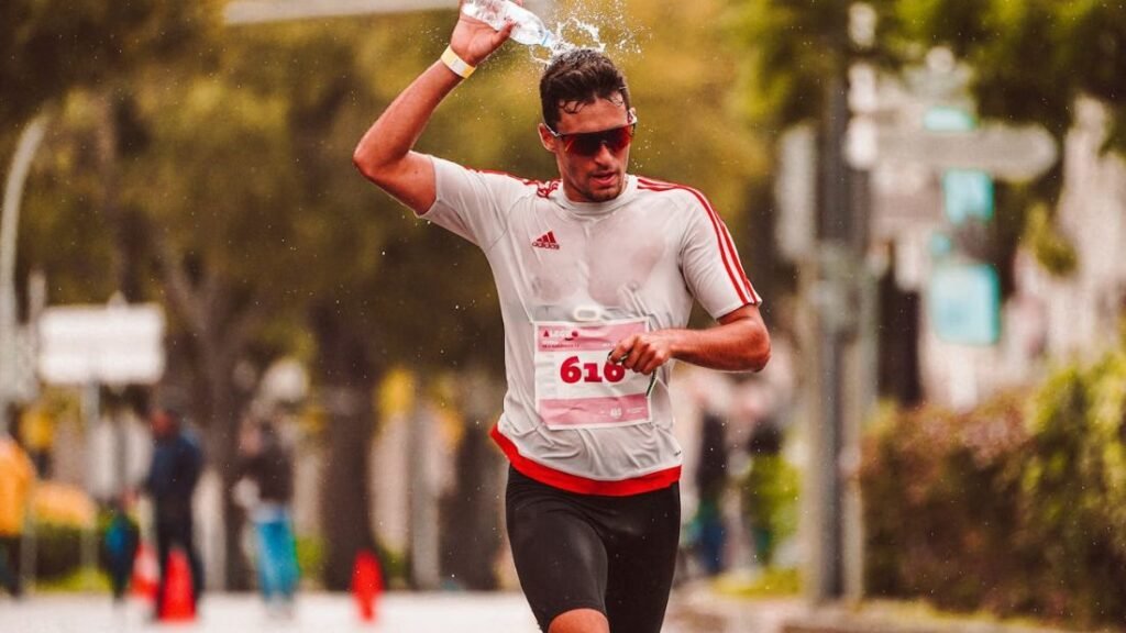 A marathon runner pouring water over their head during a race, highlighting fluid loss and cooling during intense exercise for Hydration Essentials