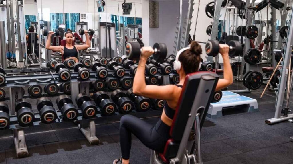 Woman performing a dumbbell shoulder press in a gym