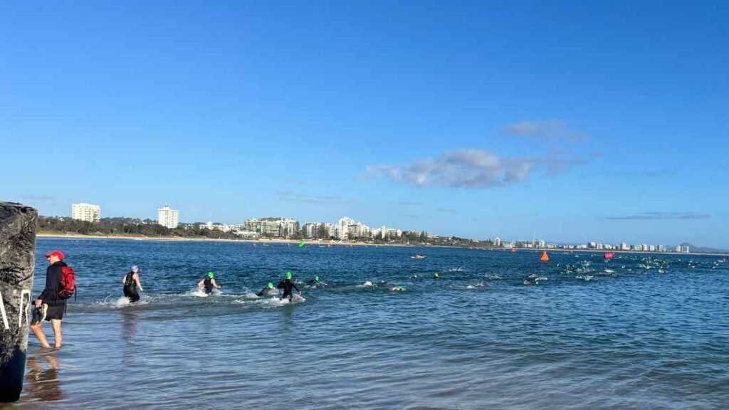 Lots of people swimming in the ocean, starting there half Ironman triathlon race.